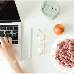 Person using a laptop on a desk with Happy Munch Yogurt Cluster Strawberry splash, an apple, and glasses
